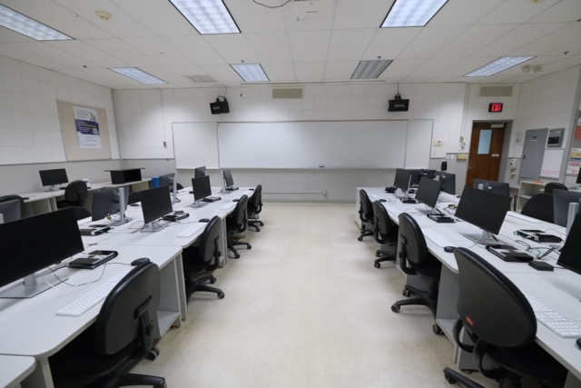 Empty university computer lab with rows of monitors, swivel chairs, and front whiteboard photo