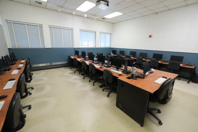 Empty classroom-style computer lab with rows of monitors and swivel chairs