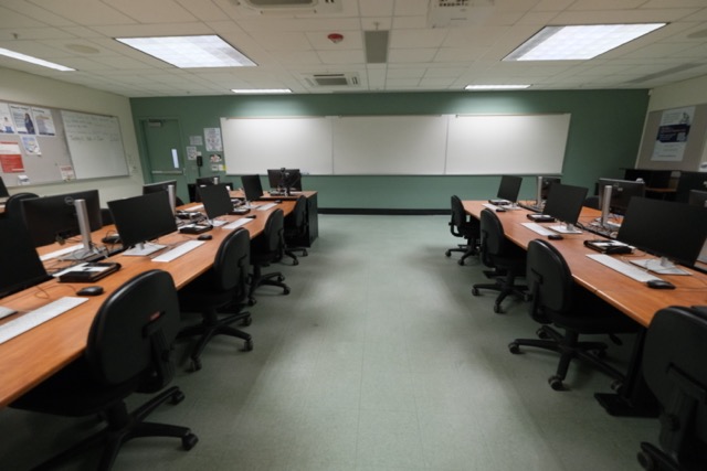 Empty computer lab with rows of monitors and chairs, green walls and whiteboard