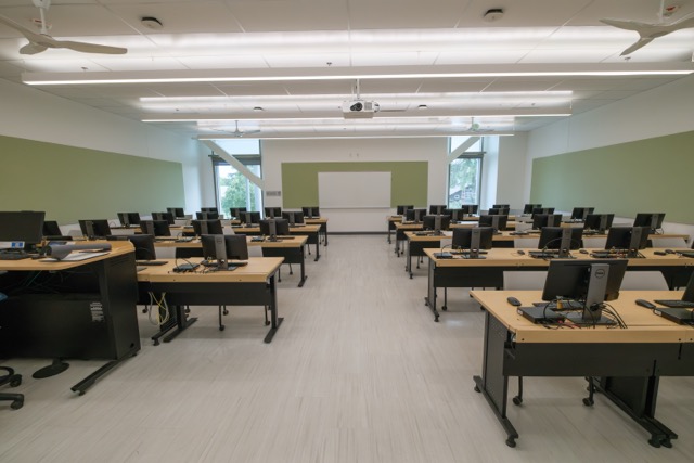 Empty computer lab with rows of desktop PCs, chairs, and a front projection screen