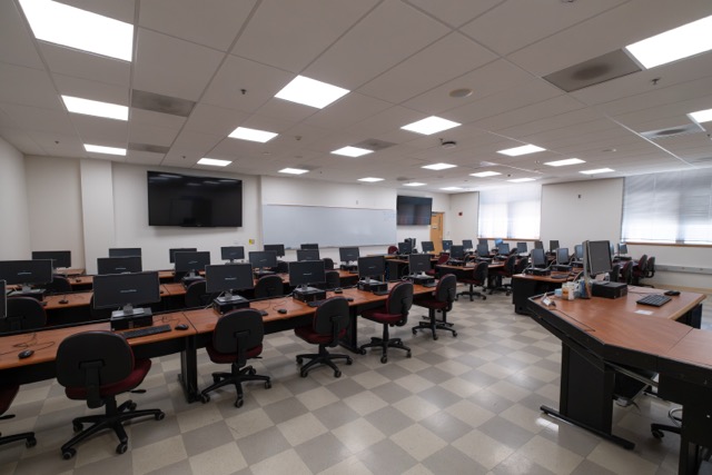 Empty computer classroom with rows of desks, monitors, and swivel chairs