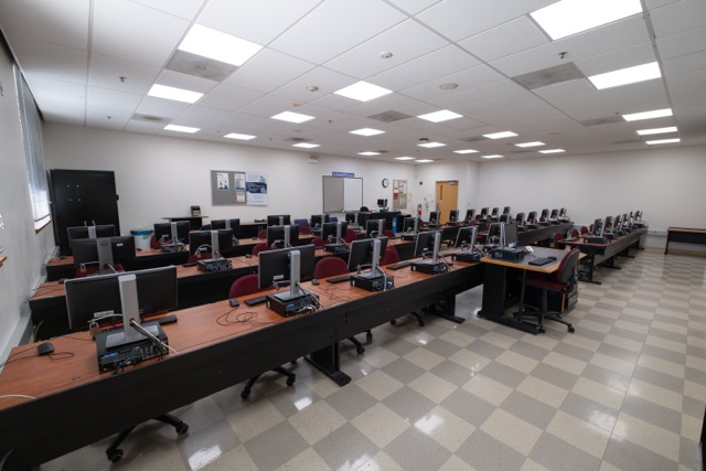 Empty computer lab with rows of desktop monitors and chairs