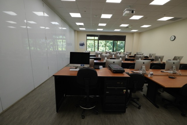 Empty computer lab with rows of desktop monitors, large whiteboard wall, and window view