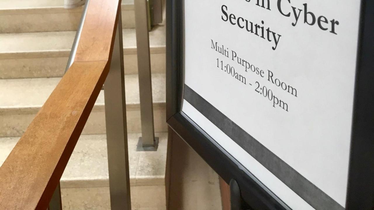 Sign for cybersecurity event, with student on stairs in background