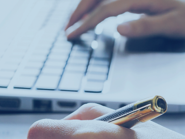 Closeup of hands on a keyboard and holding a pen